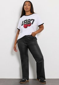 Vit t-shirt med svarta ärmar, med ett grafiskt tryck av "1987" och röda körsbär. Svarta läderbyxor och svarta skor med vita ränder.