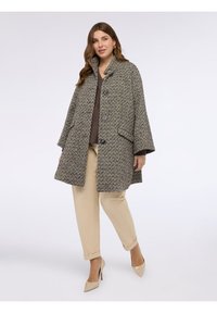 Cappotto intrecciato in un motivo a spina di pesce marrone e crema, con colletto alto, due bottoni e tasche laterali. Abbinato a pantaloni beige.