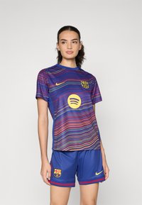 FC Barcelona fotbollskit med en flerfärgad randig tröja i nyanser av blått, rött och gult, kombinerat med blå shorts och logotypaccenter.