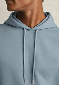 Felpa leggera blu con cappuccio, dotata di laccio e punte in metallo argentato, caratterizzata da una texture morbida e liscia e una vestibilità comoda.