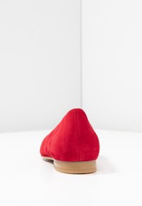Ballerines en daim rouge avec un bout pointu et une semelle lisse beige clair. La texture semble douce et mate. Design minimal sans embellissements.