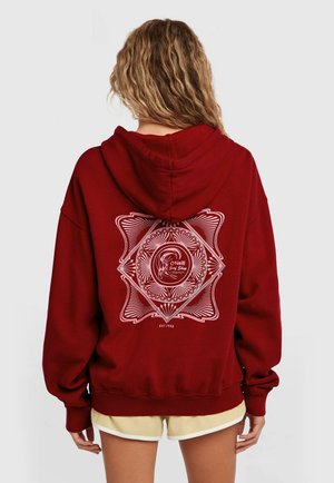 Bordeauxrode hoodie met een groot wit grafisch ontwerp op de achterkant, bestaande uit een ronde centrale logo en gedetailleerde lijnpatronen. Zachte, comfortabele pasvorm.