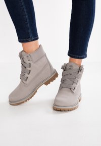 Gray ankle boots with a smooth leather upper, elastic laces, and a textured brown rubber sole. Lightly padded collar and logo on the tongue.