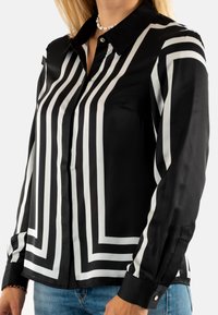 Camisa a rayas blancas y negras con acabado satinado, que presenta un cuello, mangas largas y acentos en los puños, diseñada con líneas verticales audaces.