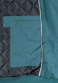 Doublure matelassée noire de veste avec poche en tissu bleu sarcelle et ourlet côtelé, montrant les détails intérieurs et les coutures du vêtement d'extérieur.