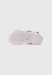 Hvite sandaler med såle som har teksturert grep og svak hæl. Har subtile dekorative detaljer og justerbare remmer på overdelen. Flat, glatt design.