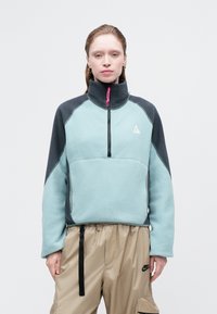 Fleece pulover z visokim ovratnikom, telo v mint zeleni barvi, sivi rokavi, sprednji del na pol zadrgo in rožnato zadrgo; vsebuje logotip na prsih.