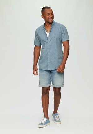 Chemise à manches courtes bleu à boutons avec un motif texturé, associée à un short en denim clair et des baskets bleues. Tenue d'été décontractée.