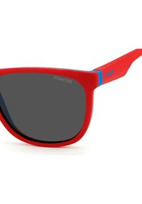 Lunettes de soleil en plastique rouge avec des verres gris et des accents bleus sur les branches. Présente un design moderne et angulaire avec une finition mate.
