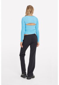 Maglione azzurro chiaro a coste con un particolare taglio sulla schiena, abbinato a pantaloni neri e scarpe nere chunky.