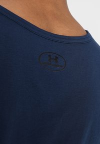 Laivastonsininen puuvillainen t-paita pyöreällä pääntiellä ja mustalla logotilkulla takana. Sileä pinta, hengittävä kangas, rento istuvuus.