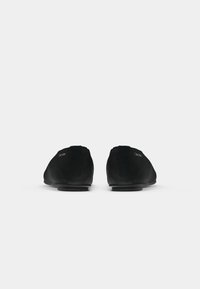 Een paar zwarte slip-on schoenen van Calvin Klein, achteraanzicht, op een effen witte achtergrond.