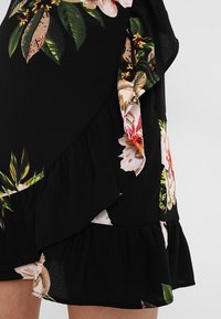 Czarna sukienka w kwiaty z falbanką u dołu i nałożonym wzorem z kolorowymi kwiatami oraz zielonymi liśćmi, wykonana z lekkiego materiału.