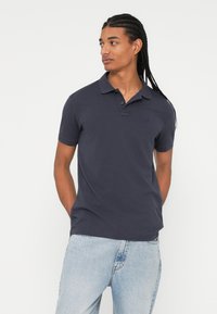 Marineblå polo shirt lavet af bomuld, med en klassisk krave, korte ærmer og et syet logo på venstre bryst.