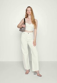 Top branco curto, calças largas brancas, mala com padrão de zebra e sandálias de salto preto e branco. Cabelo longo estilizado em ondas soltas.