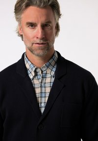 Námořnický svetr s jedinou kapsou přes světle modrou a béžovou kostkovanou košili, která má límeček na knoflíky a texturovanou tkaninu.