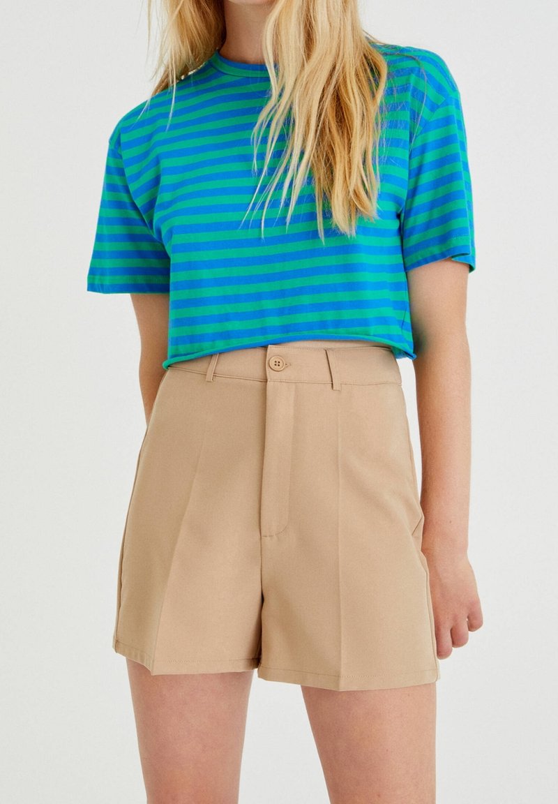 Maglietta a maniche corte a righe blu e verdi abbinata a pantaloncini beige a vita alta con bottoni frontali e design su misura.