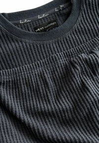 Dunkelgraues Umstandoberteil aus geripptem Stoff. Mit Rundhalsausschnitt und strukturiertem Design mit dezenten Fältchen unter der Brust.