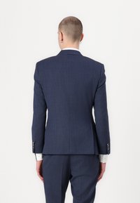 Navy blue tailored suit with subtle texture, slim fit, and single vent at the back. Features silver buttons on the sleeves and white shirt cuffs.