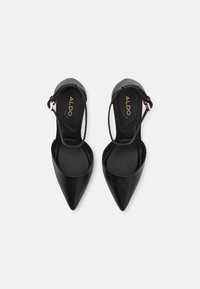 Chaussures à talon aiguille noires avec une finition en cuir lisse, des côtés ouverts et un accent en boucle dorée. Design plat et style minimaliste.