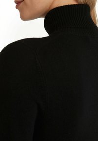 Czarny sweter z golfem, z widokiem zbliżeniowym na szwy pleców i ramion. Miękka faktura i dopasowany fason.