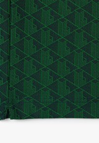 Zelená látka se geometrickým vzorem opakujících se diamantových tvarů. Design zahrnuje stylizované svislé linky, které vytvářejí strukturovaný efekt.