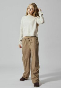 Pull en tricot gris clair à manches longues, associé à un pantalon ample à rayures marron et crème. Texture douce, taille élastique et poches.