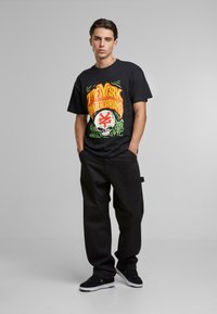 Sort grafisk t-shirt med et farverigt skateboarddesign, parret med løse sorte bukser og sorte sneakers med hvide såler.