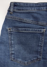 Dark blue denim jeans featuring a back pocket with a hidden rivet, visible stitching, and a smooth texture. No branding is visible.