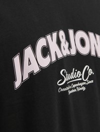 Sort bomuld t-shirt med et dristigt hvidt grafisk tekstdesign, der læser "JACK&JON" og "Studio Co." med en glat tekstur.