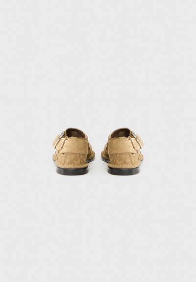 Παπούτσια από σουέτ σε μπεζ χρώμα με χαμηλό προφίλ, διαθέτοντας στρογγυλεμένη μύτη και διακοσμητικό λουράκι. Μαύρη λαστιχένια σόλα με διακοσμήσεις ραφής.