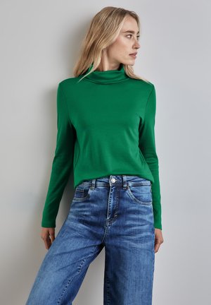 Green long-sleeve turtleneck top, smooth fabric, paired with wide-leg, light blue denim jeans featuring a button closure and pockets.
