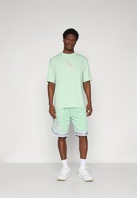 Conjunto em verde menta composto por uma t-shirt de mangas curtas com um logótipo e calções com detalhes florais e acabamento branco. Feito em tecido de algodão.