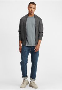 Mørk grå ripet cardigan over en lys grå skjorte, kombinert med oppbrettede blå jeans og beige sneakers. Enkel design, uformell passform.