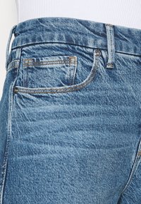 Vaqueros de mezclilla azul con un acabado texturizado, diseño de cinco bolsillos, detalles cosidos y una cintura alta, que capturan un efecto de lavado claro.