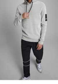 Sudadera con capucha gris claro con textura, capucha y cordones negros, combinada con pantalones negros ajustados con detalles blancos y zapatillas blancas.