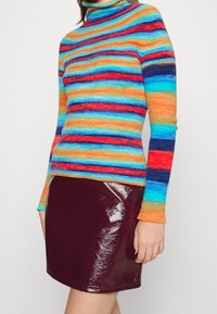 Femme portant un pull à col roulé à manches longues rayé de couleurs vives et une mini jupe bourgogne brillante.