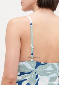 Maillot de bain une pièce avec un motif floral en bleu et vert, doté de bretelles ajustables et d'un dos plongeant. Comprend un tatouage visible.