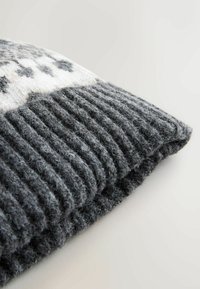 Gray knit sweater showing a textured ribbed hem. The upper part features a smooth, light gray and white pattern with dark accents.