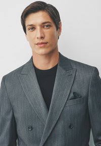 Grau gestreifter, doppelt gefütterter Blazer mit einer Satin-Taschentuch und einem schwarzen Rundhals-Unterhemd, das eine glatte Textur und eine strukturierte Passform aufweist.
