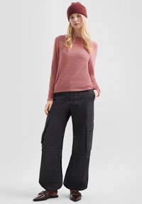 Rosa gestreiftes Langarmshirt und schwarze Cargo-Hosen mit Leopardenmuster. Enthält strukturierten Stoff und seitliche Taschen. Braune flache Schuhe.