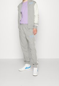 Grå sweatshirt med vita ärmar och blå detaljer, tillsammans med grå byxor med sidostenar och matchande logotyp, bärs med vita skor.