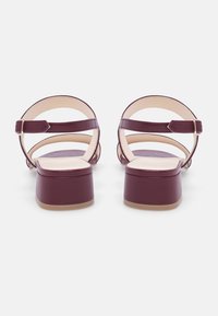 Sandali Marlowe con tacco a blocco in pelle bordeaux, dotati di cinturini regolabili e solette beige lisce. Il design con tacco a blocco offre stabilità.
