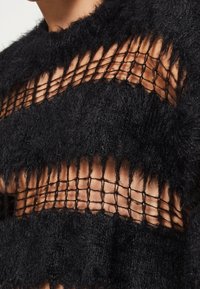 Black knit sweater featuring fuzzy texture with horizontal cutouts and a net-like pattern. Edges are unfinished, creating a fringed effect.