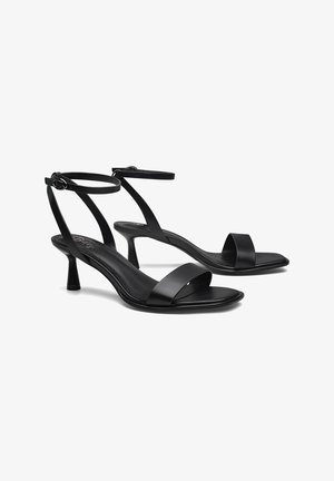 Sandalias negras de tacón alto con un diseño minimalista, que presentan tiras delgadas en el tobillo, punta abierta y material de cuero suave. Altura del tacón de 7,5 cm.