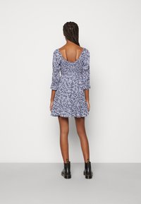 Blå blommig klänning med trekvartslånga ärmar, smockad baksida och en utsvängd fåll. Bärs med svarta ankelboots för kontrast.