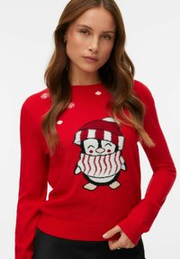 Sarkans adīts džemperis ar pingvīna grafiku, kuram ir svītrains šalle un cepure, papildināts ar baltām sniegpārsliņu rakstiem priekšpusē.