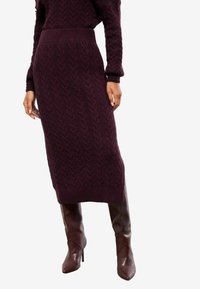 Bordeauxfarvet strikket kjole med et tekstureret kabelmønster, der har en tætsiddende talje og ribbet kant. Kombineret med knæhøje brune læderstøvler.
