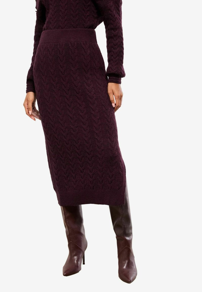 Bordeauxfarvet strikket kjole med et tekstureret kabelmønster, der har en tætsiddende talje og ribbet kant. Kombineret med knæhøje brune læderstøvler.