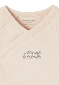 Hellbeige Babykombination mit Wickelausschnitt, bedruckt mit "petit amour de la famille" in geschwungenem Schriftzug auf der Brust.